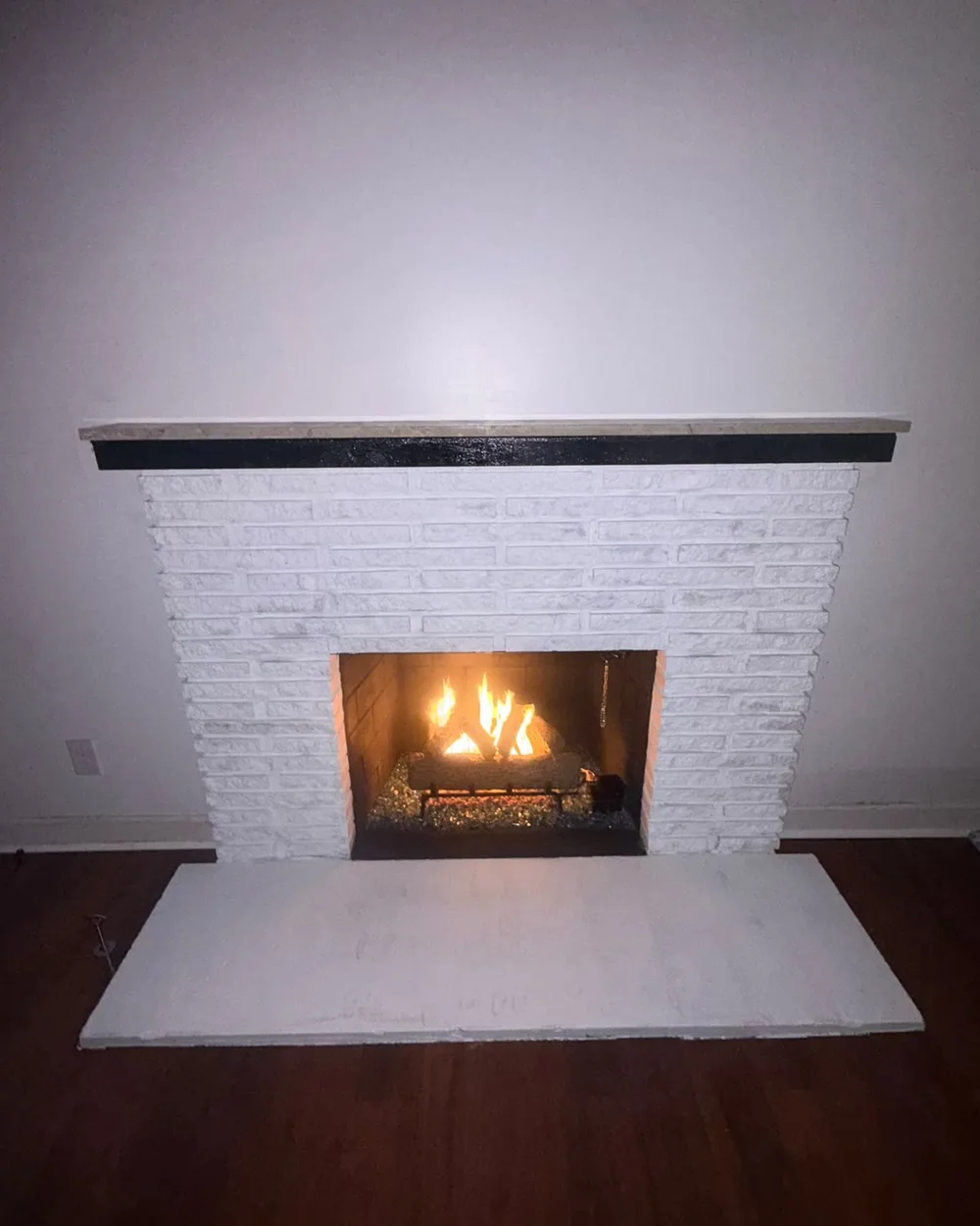 Finished white brick fireplace with a fire burning